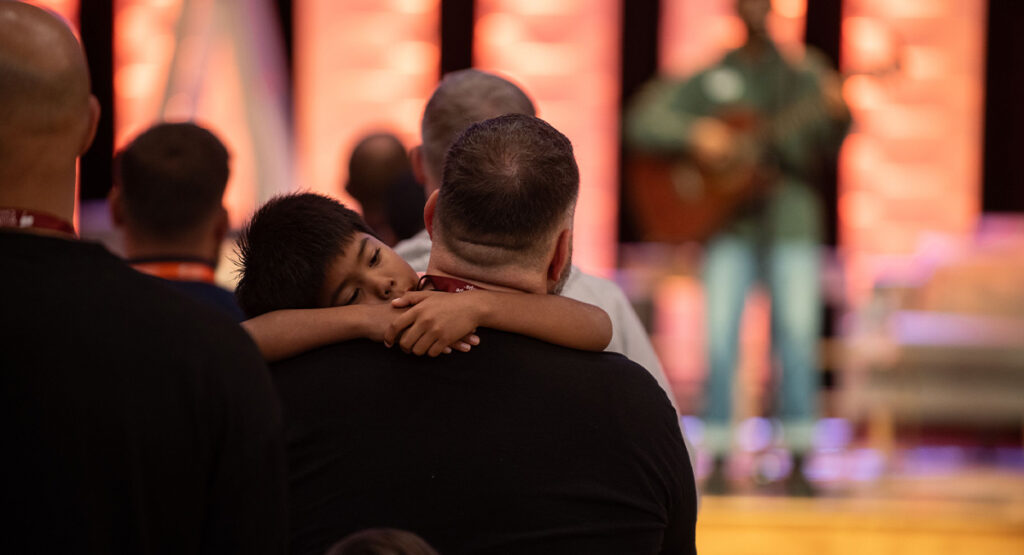 abundant living, dad and son at worship session hugging